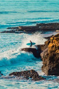 Surfer on the rocky coastline of Taghazout with waves crashing