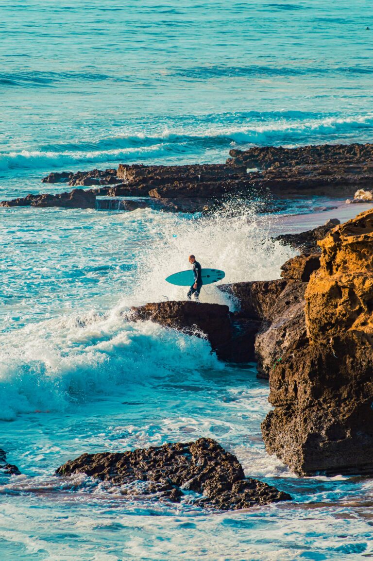 Surfer on the rocky coastline of Taghazout with waves crashing
